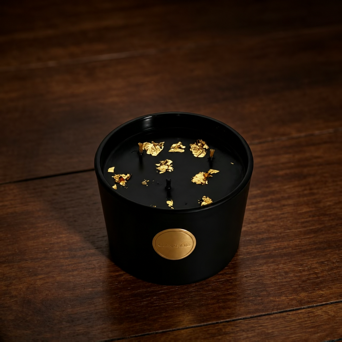 Black and gold three-wick soy candle on a dark wood surface