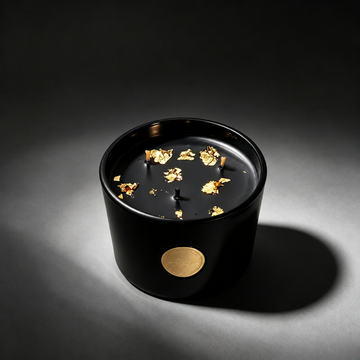 Black and gold three-wick soy candle with gold foil flakes under a soft spotlight