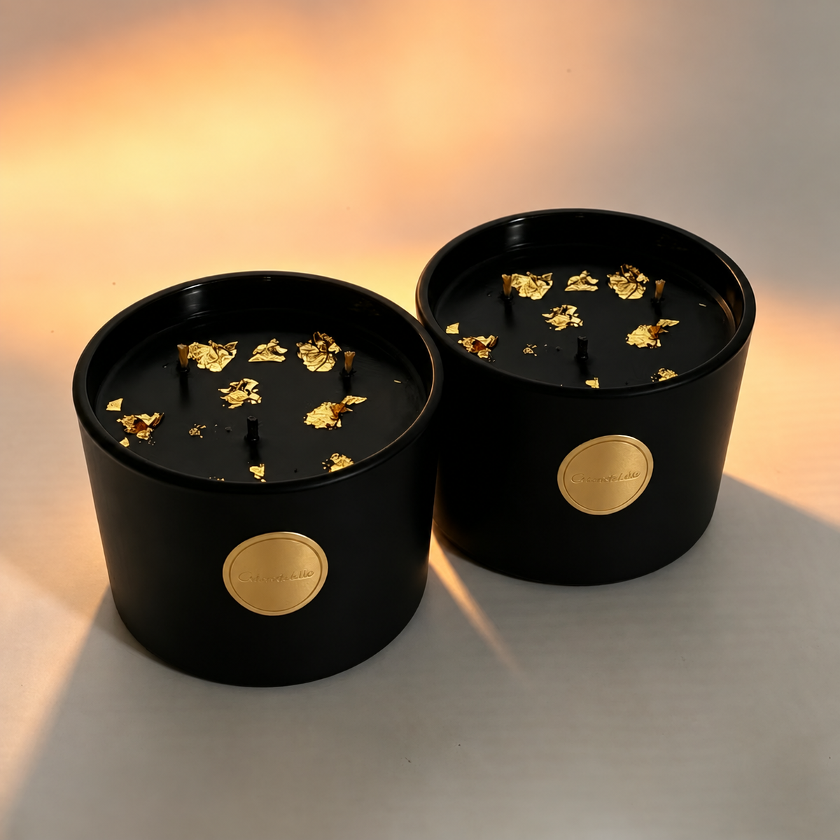 Two black and gold three-wick soy candles with gold badges in warm light