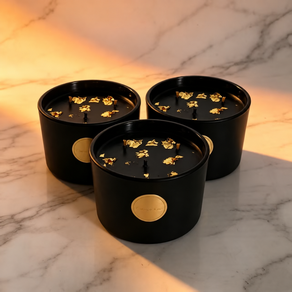 Three black and gold three-wick soy candles on a white marble surface