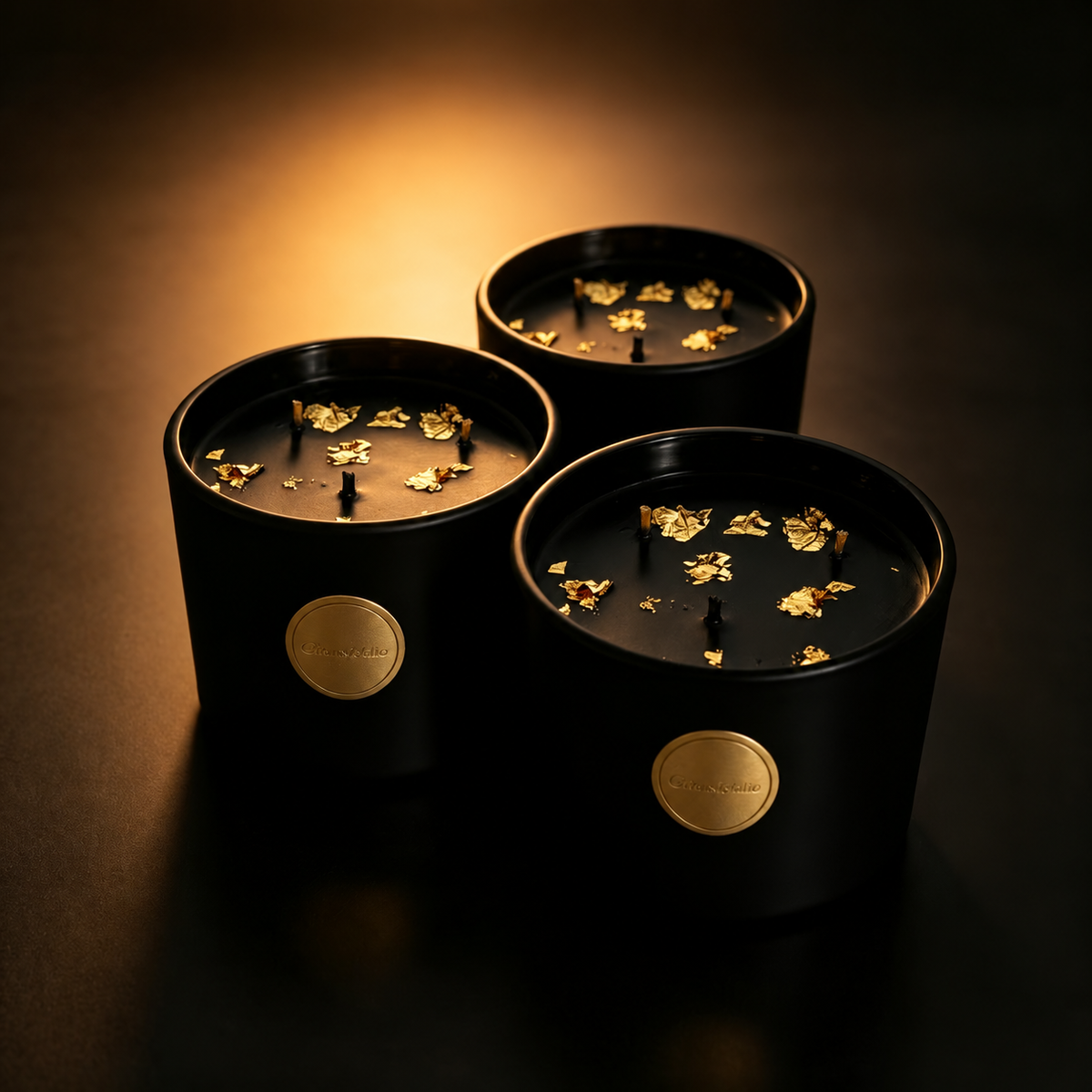 Three black and gold three-wick soy candles against a dark backdrop with a warm glow