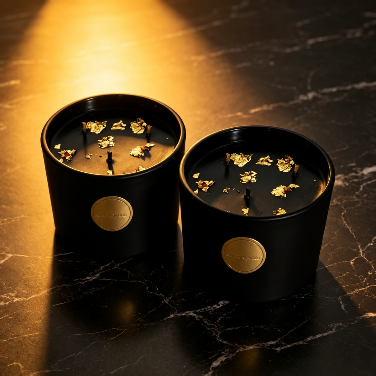 Two black and gold three-wick soy candles on black marble